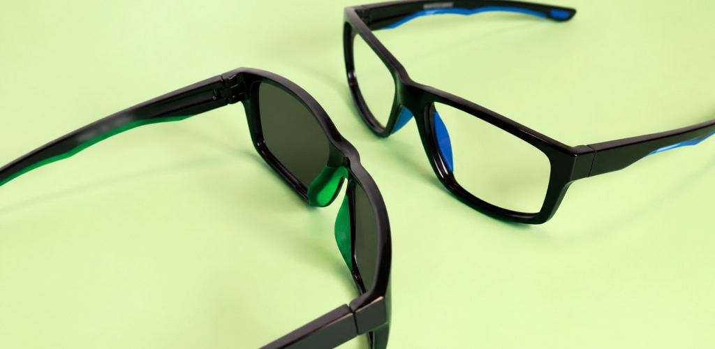 Black wraparound Harrington Sport sunglasses with tinted lenses facing black running glasses with clear lenses, both on a light-green background.