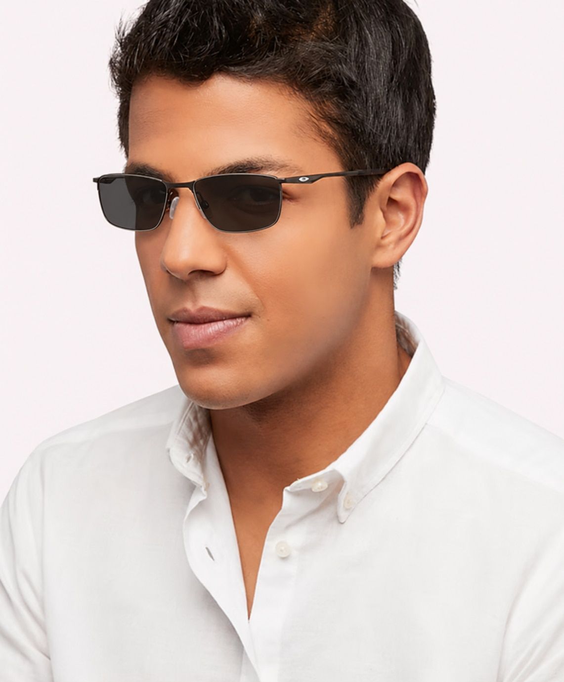 A man with short dark hair wears semi-rimless Oakley Socket 5.5 sunglasses and a crisp white shirt, posed against a clean studio background.
