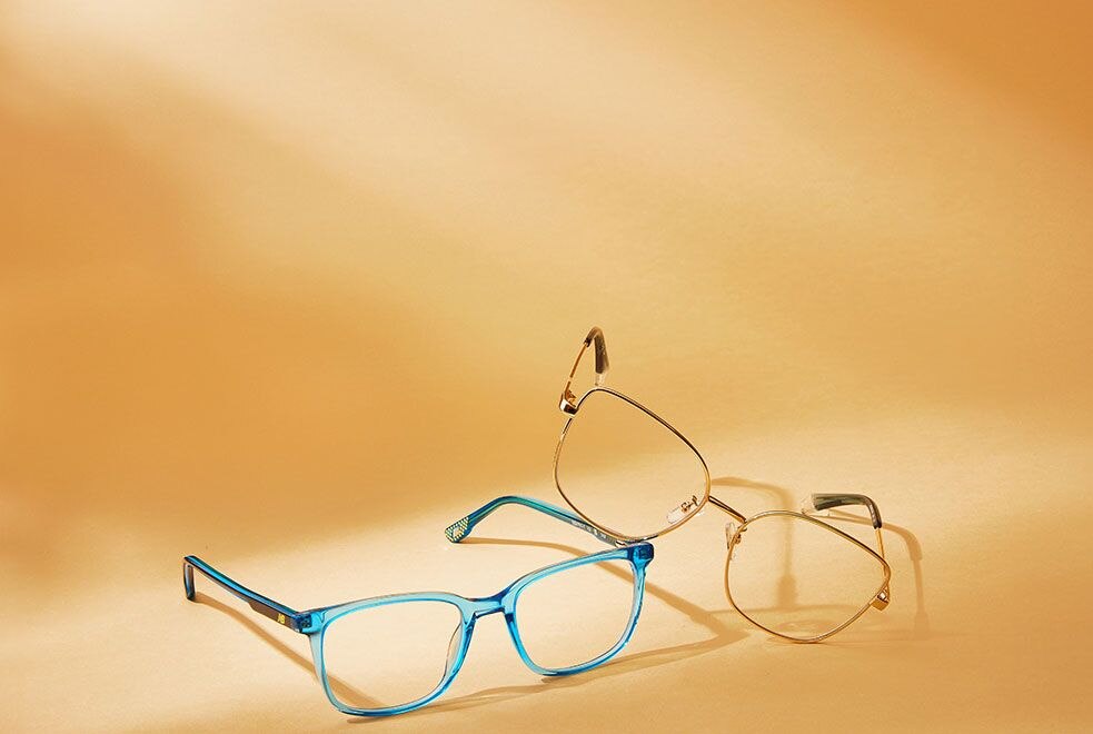 A blue pair of acetate frames and a pair of metal frames lying next to each other on a yellow background
