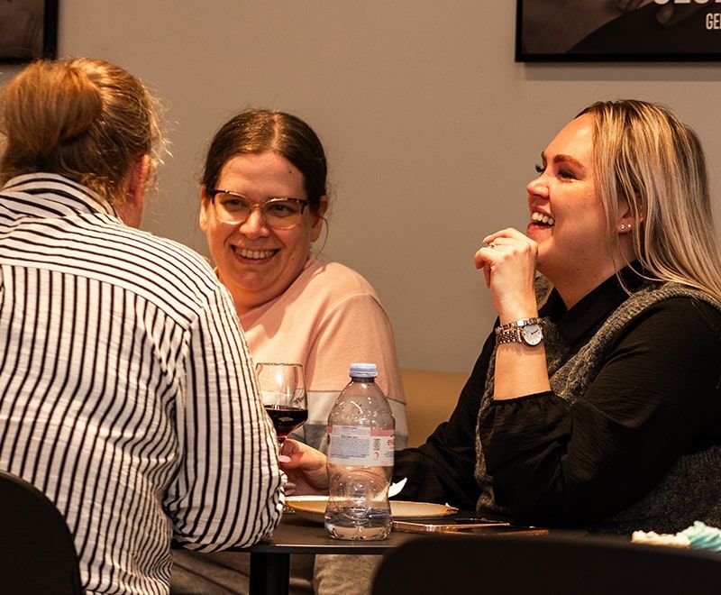 3 females laughing at a table while having drinks