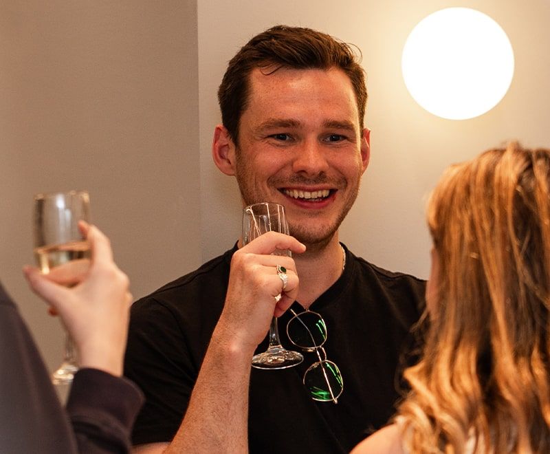 Close-up of male smiling amongst two females while hold a drink