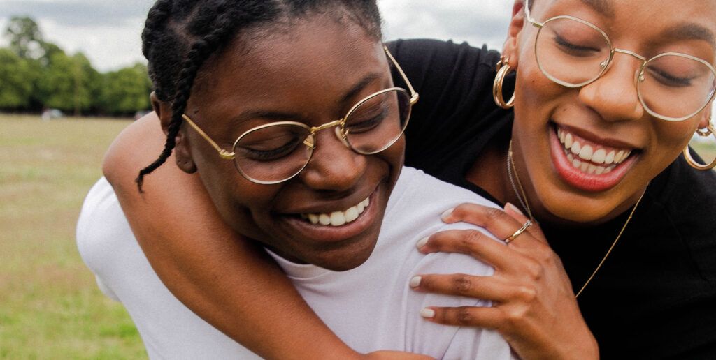 Two young people wearing gold-rimmed glasses, hugging and laughing together