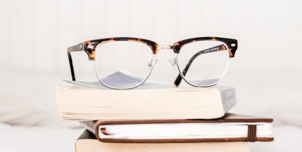 A pair of Ray-Ban Clubmaster glasses lying on top of a stack of books