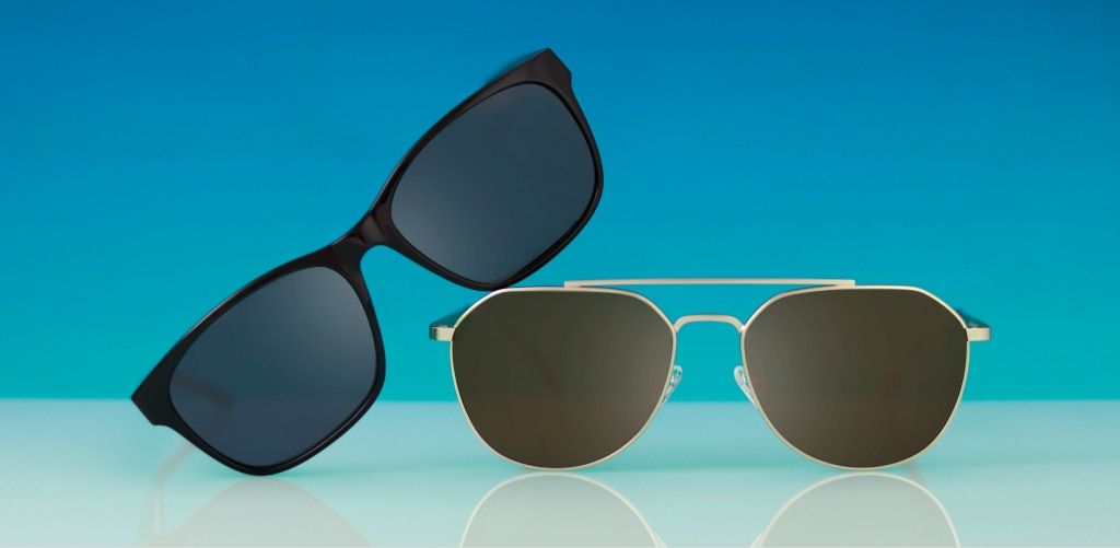 GD Collection Colby and Aero sunglasses are displayed against a bright blue background. On the left, the GD Aero sunglasses feature black acetate rectangular frames with dark grey lenses and lean diagonally. On the right, the GD Colby sunglasses have a go