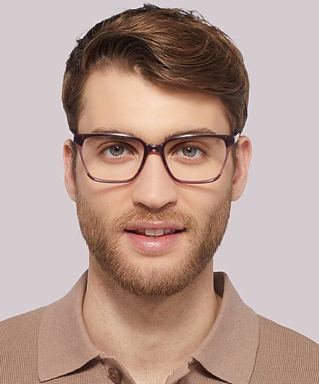 Close-up of a man wearing purple rectangular glasses, with short strawberry-blonde hair and a trimmed beard, against a plain background.