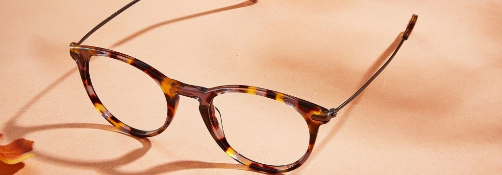 A retro-style round frame with metal temples on a peach-coloured surface with orange leaves peeking from the corners.