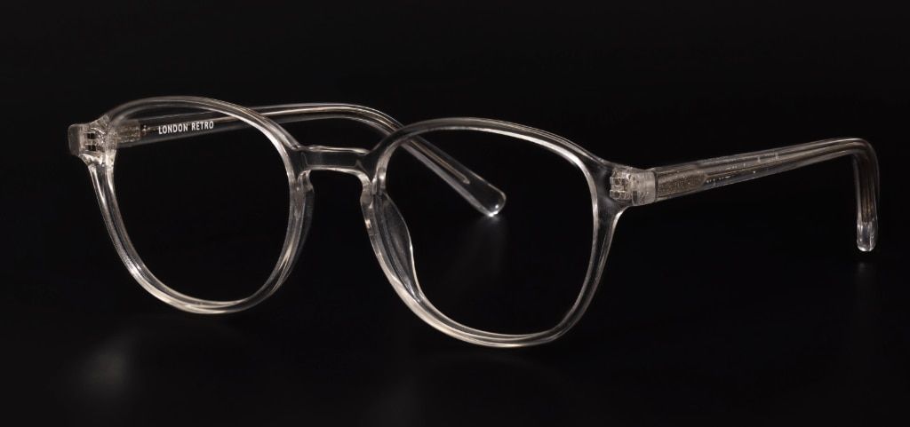 A pair of transparent road glasses made of acetate with a keyhole bridge. They are standing up to one side on a plain black background.