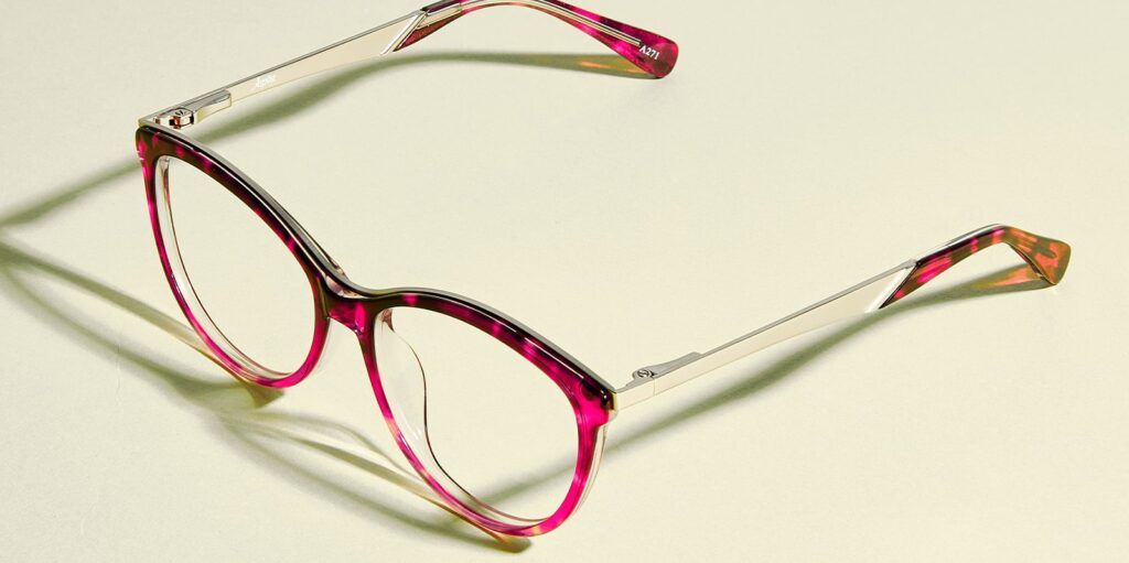Round, pink tortoiseshell Aspire frame with silver arms facing bottom left on a pale green background