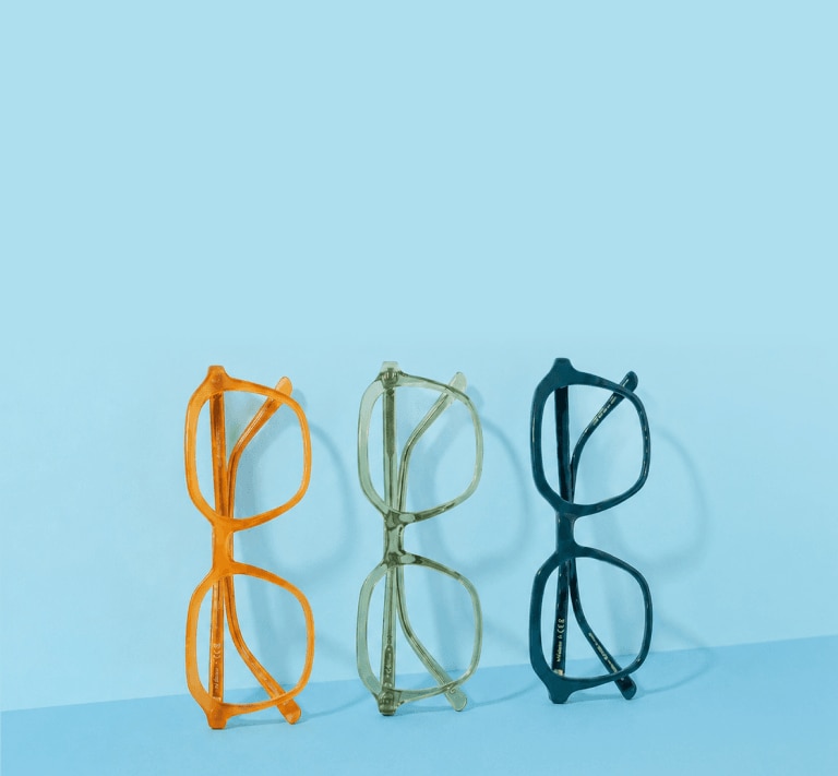Three pairs of colourful glasses frames leaning sideways against a blue wall