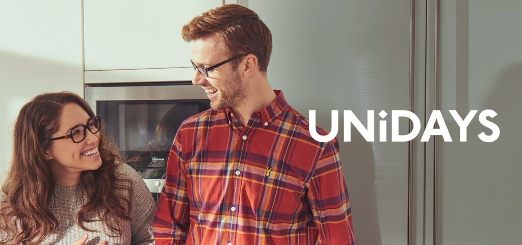 Two young students, one male and one female wearing frames looking at one another amiling with the UNIDAYs logo added to the image
