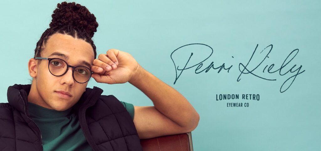Young male wearing round glasses, holding the side of the frame with their hand, with the Perri Kiely X London Retro logo