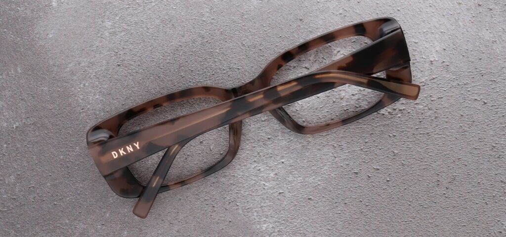 Close-up shot of a pair of DKNY rectangular tortoiseshell frames laid on thier front with the arms and DKNY logo showing