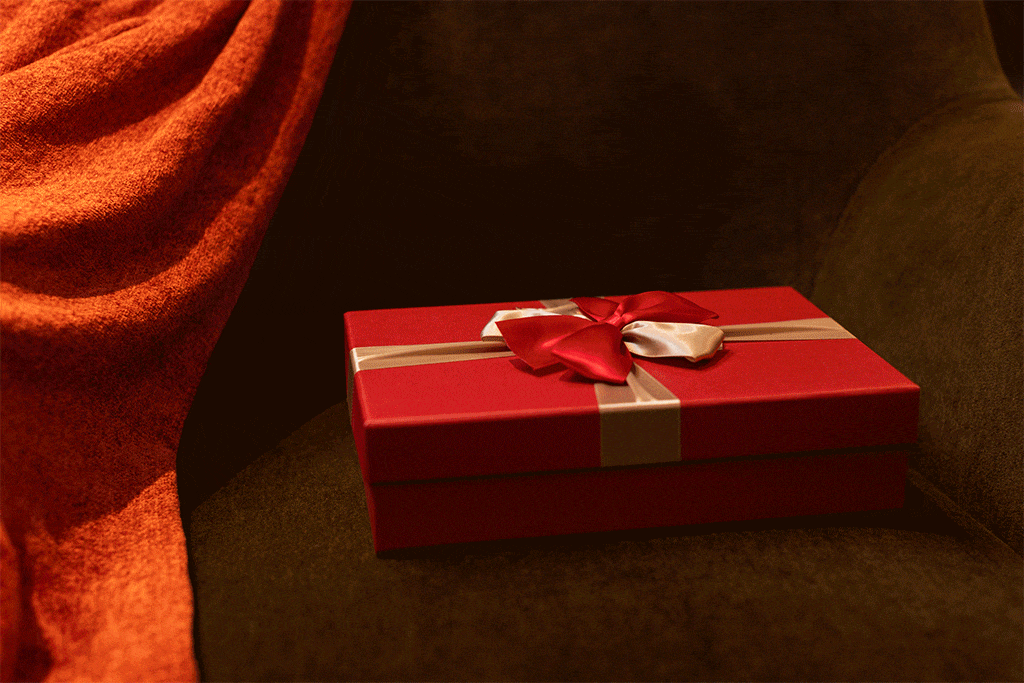 Two hands opening a surprise red Christmas present box with a bow on top.
