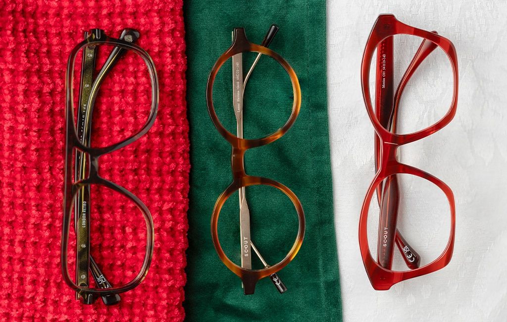 A set of three folded pairs of glasses displayed on different fabrics. The first is a Havana acetate frame resting on red knit material. The second a round Havana acetate frame with gold metal temples placed on green velvet fabric, and finally the third, 