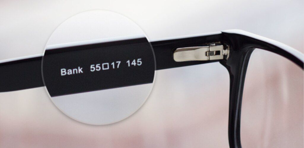 Close-up of the inside arm of a glasses frame showing frame measurements, including lens width, bridge width, and temple length, highlighted through a magnified view.