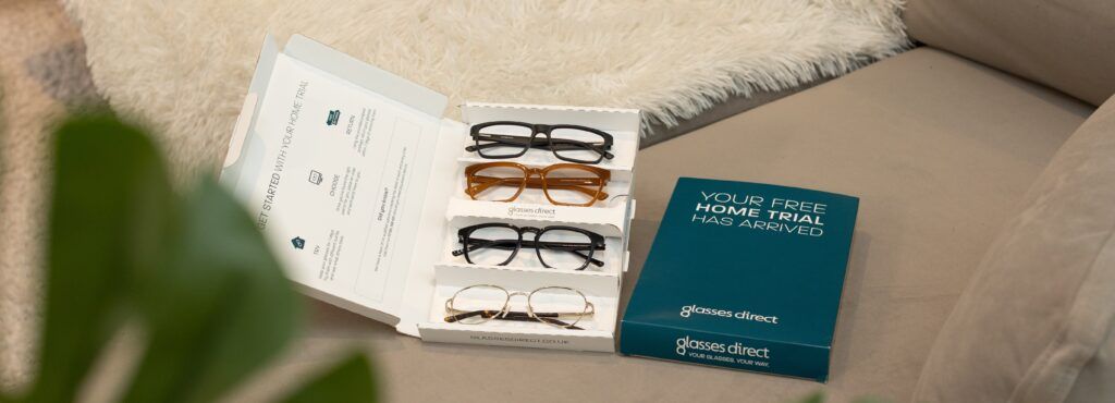 An open Home Trial glasses box from Glasses Direct resting on a grey sofa, with 4 frames inside.