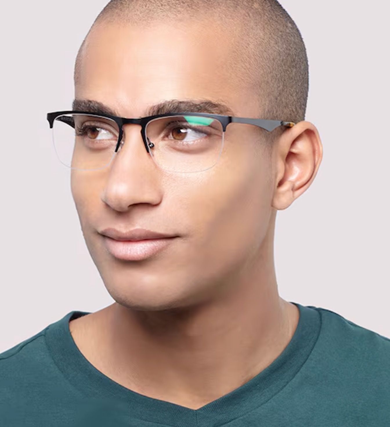A young man with a closely-cropped buzz cut. He is wearing a pair of semi-rimless rectangular glasses. The man's face is turned to his right side and he is smiling. His green t-shirt is just visible.