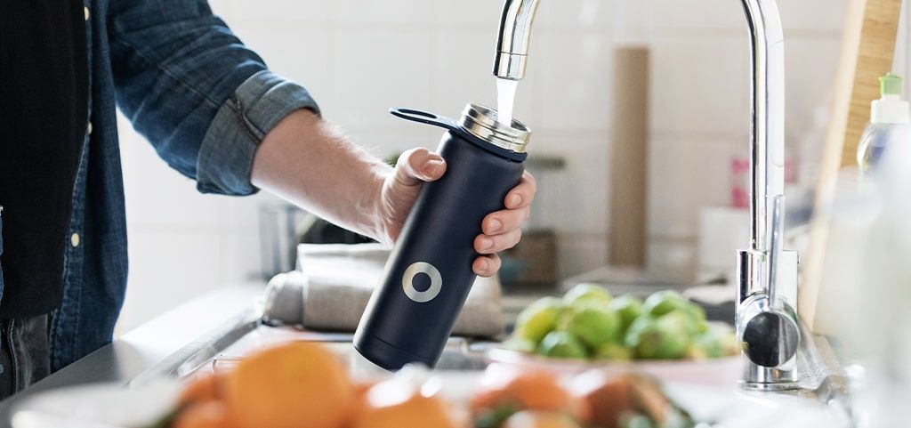 Man pouring water into bottle from tap
