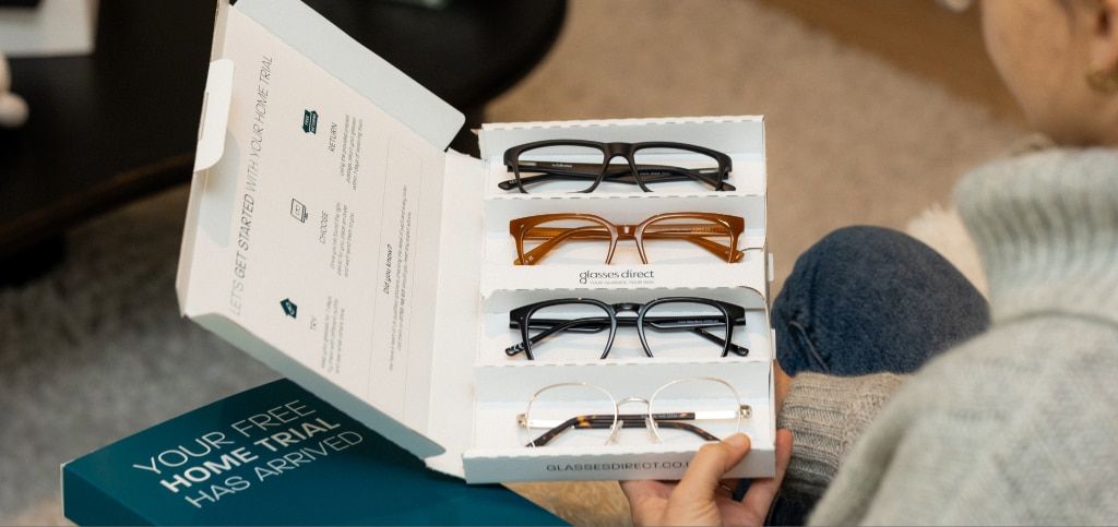 Over-the-shoulder shot of a customer opening a Glasses Direct Home Trial box, which showcases four different pairs of glasses frames, ready to try at home.