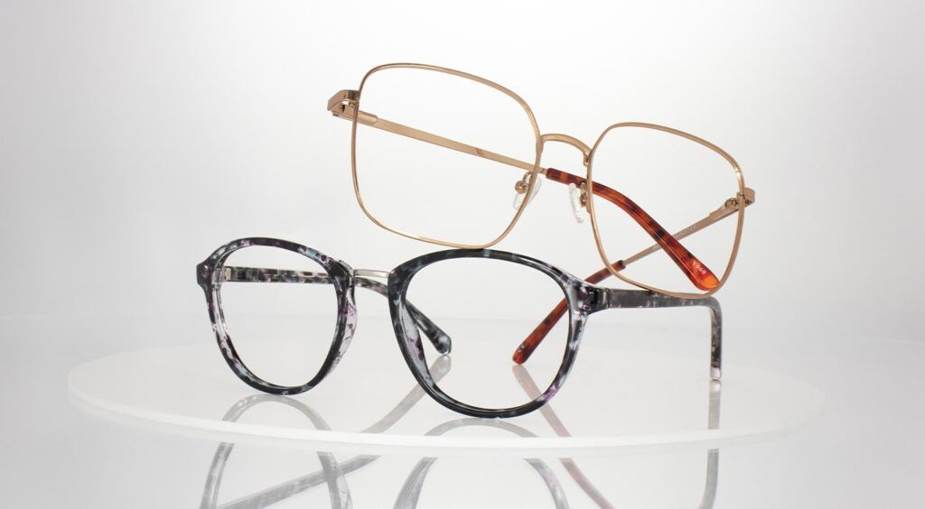 Close-up shot of 2 frames, stacked on top of one another, bottom frame is a round, black tortoiseshell frame and the top is a square, gold metal frame