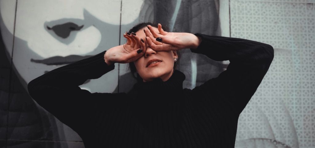 A woman standing in an artistic outdoor space covering her eyes
