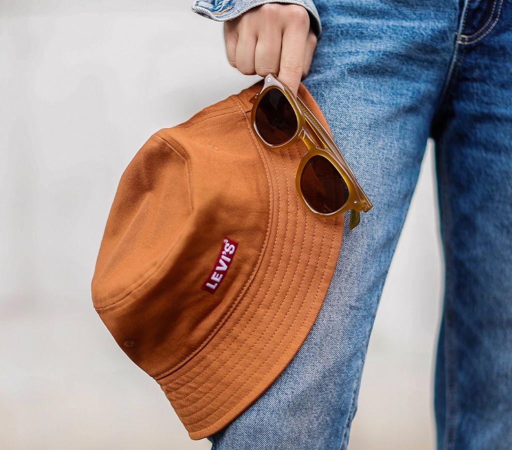Close-up shot of a woman holding an orange bucket Levi's hat and pair of orange Levi's sunglasses
