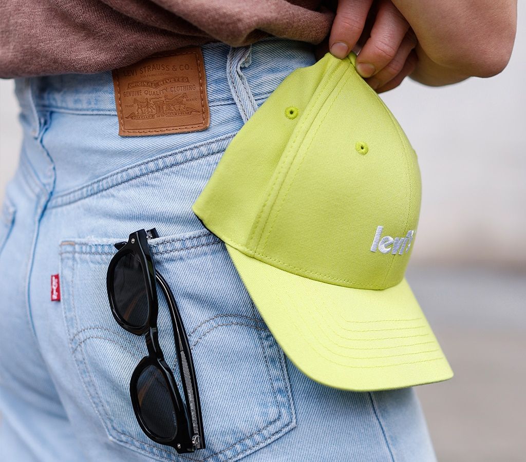 Close-up shot of a yellow Levi's cap and pair of black Levi's sunglasses sticking from a man's back pocket