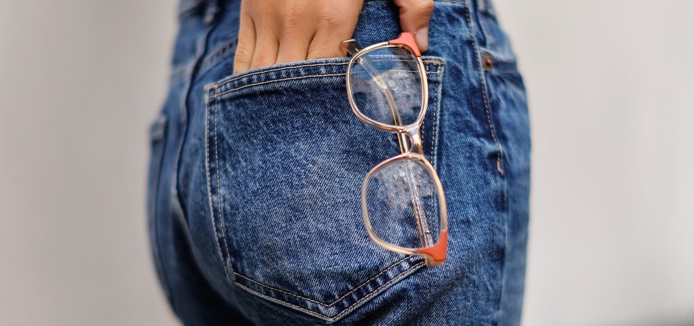 Close-up shot of square shaped Levis frames in beige with orange edges on the frames sticking from a woman's back pocket