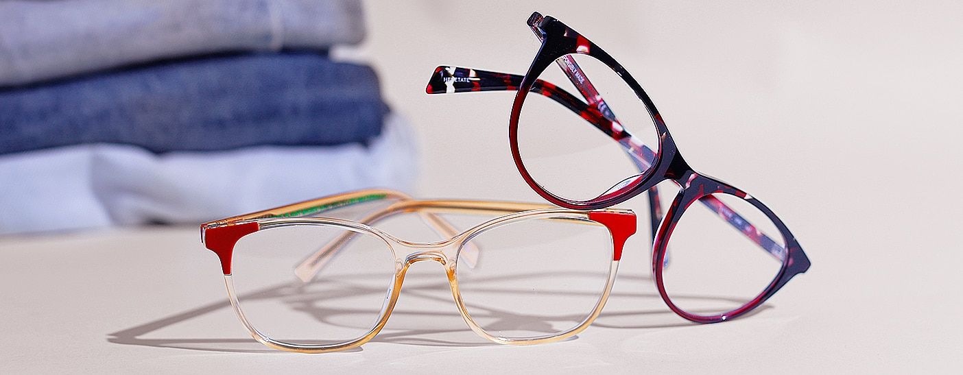 Close-up shot of 2 pairs of Levi's frames, one in beige with orange edges and the other in purple tortoiseshell, with some jeans folded up in the background
