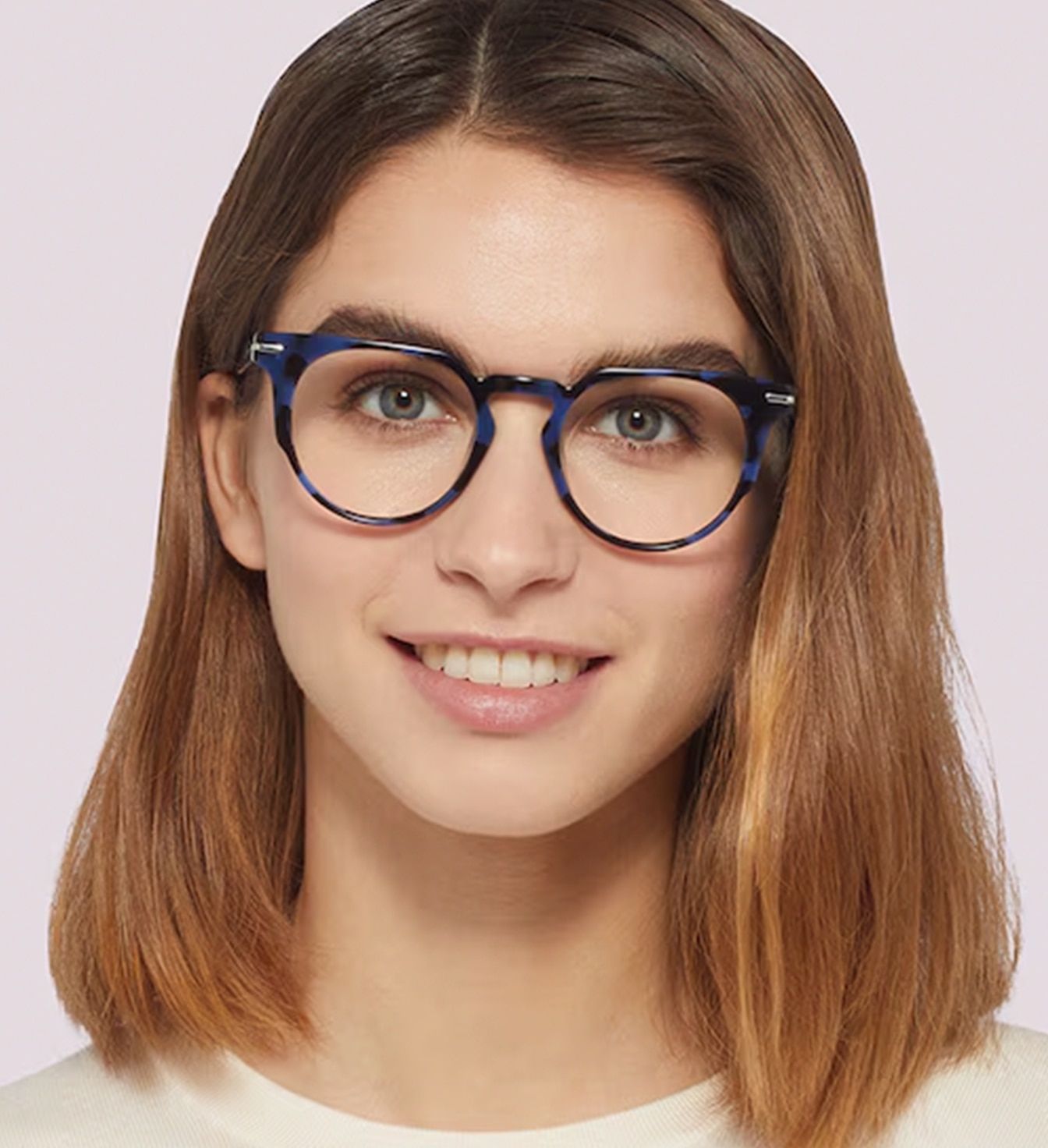 A young lady with medium dark-blonde hair smiling brightly, wearing a pair of vibrant blue acetate glasses with a quirky geometric shape.