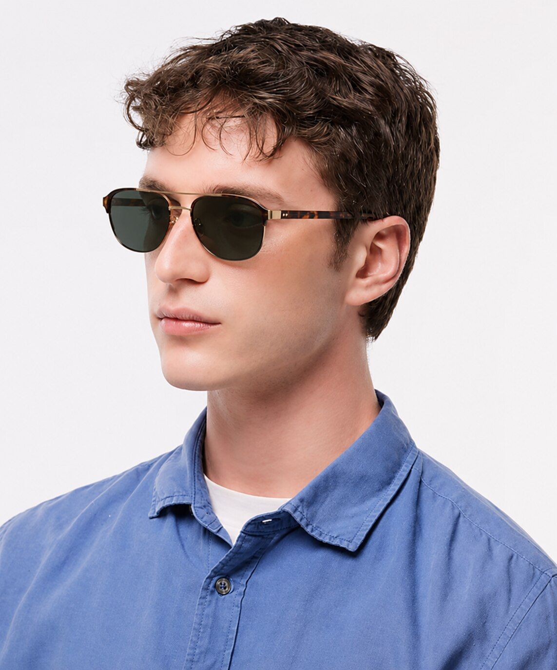 Man with short frizzy hair wearing a light-blue shirt and aviator-style London Retro Redford prescription sunglasses against a light background.