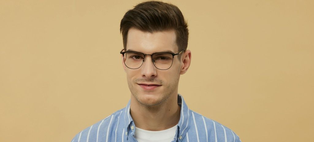 A young man with brown hair and a quiff, he is wearing a pair of black titanium glasses and a blue-and-white striped shirt. The background is a golden yellow.