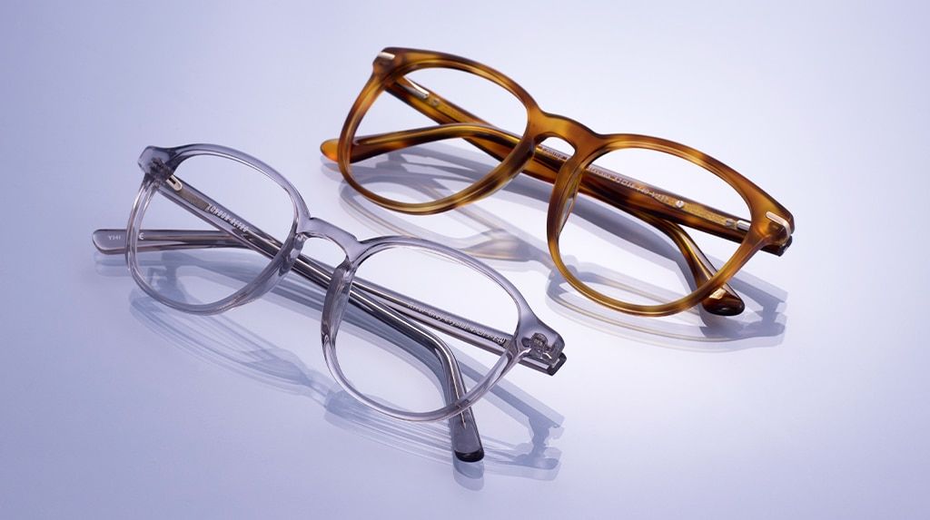 Two square acetate glasses frames set against a light purple background, both casting shadows. One is square-shaped and features a light honey Havana finish with a keyhole bridge and metal temple accents, while the other is a transparent grey design with