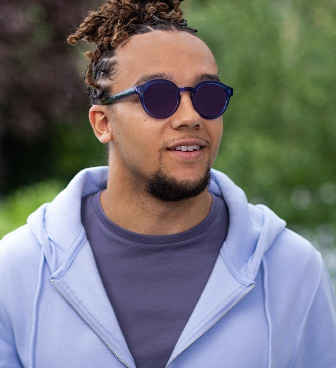 Young male wearing a pair of round, blue GD Collection frames with Amethyst Transitions tints
