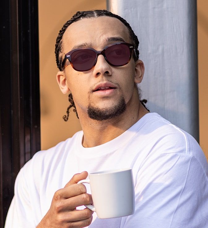 Young male wearing a pair of square, chunky, tortoiseshell Ray-Ban frames with Ruby Transitions tints