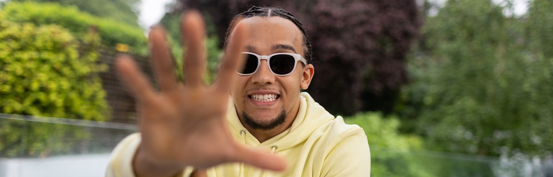 Young male smiling wearing a pair of rectangular, white GD Collection frames with Brown Transitions tints