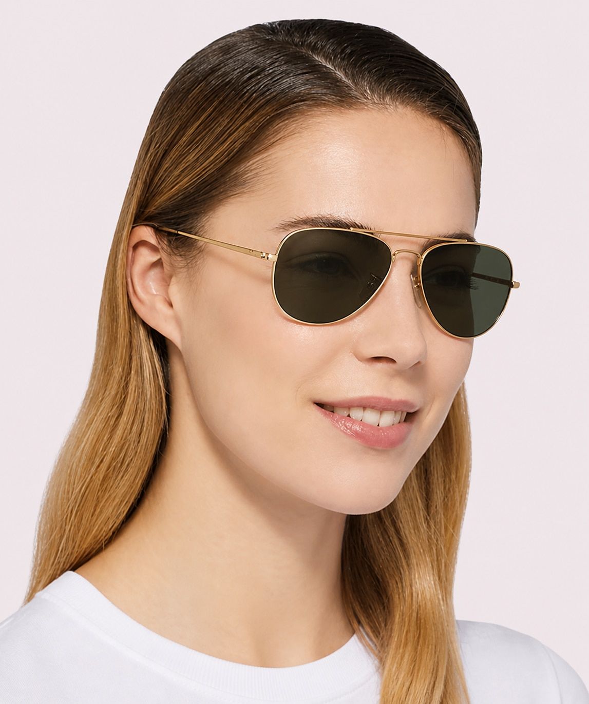 A smiling woman with long blonde hair wears a white t-shirt and gold Ray-Ban® Aviator sunglasses, posed against a clean white background.