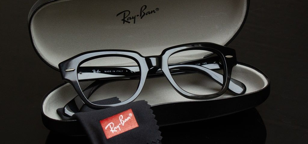A pair of shiny acetate geometric Ray-Ban glasses positioned in a black glasses case with the Ray-Ban cleaning cloth neatly folded by it.