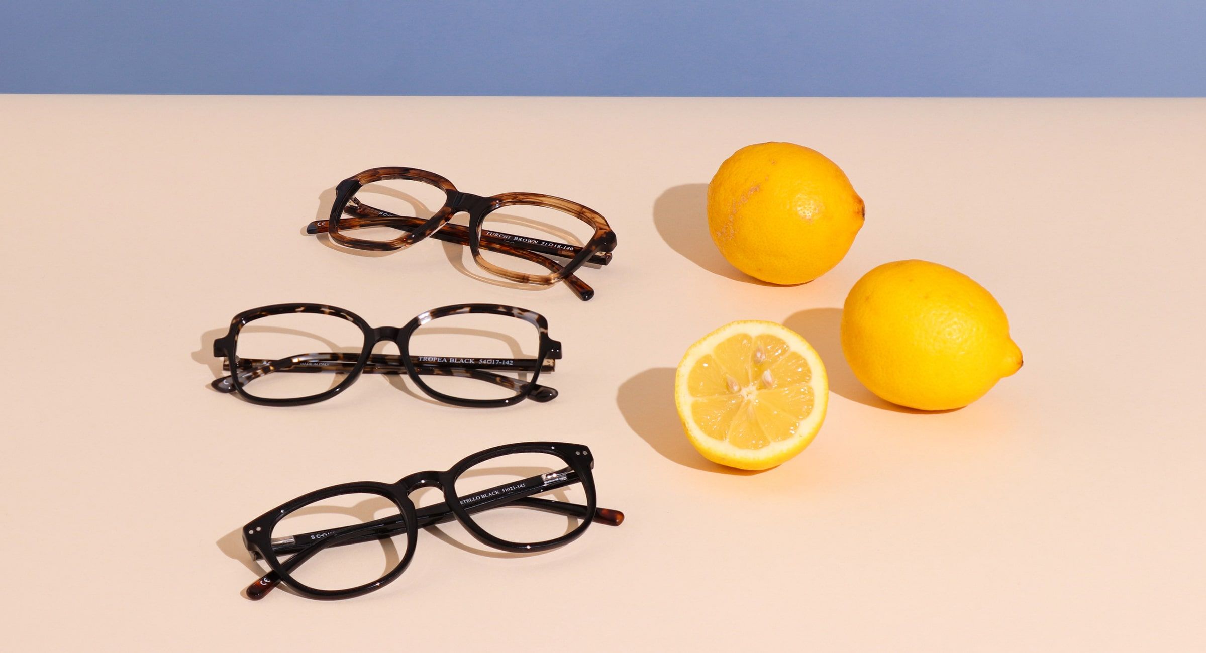 3 pairs of Scout: Made in Italy frames on a beige and yellow background, one frame in its hardcase surrounded by 2 whole lemons and sliced half of a lemon