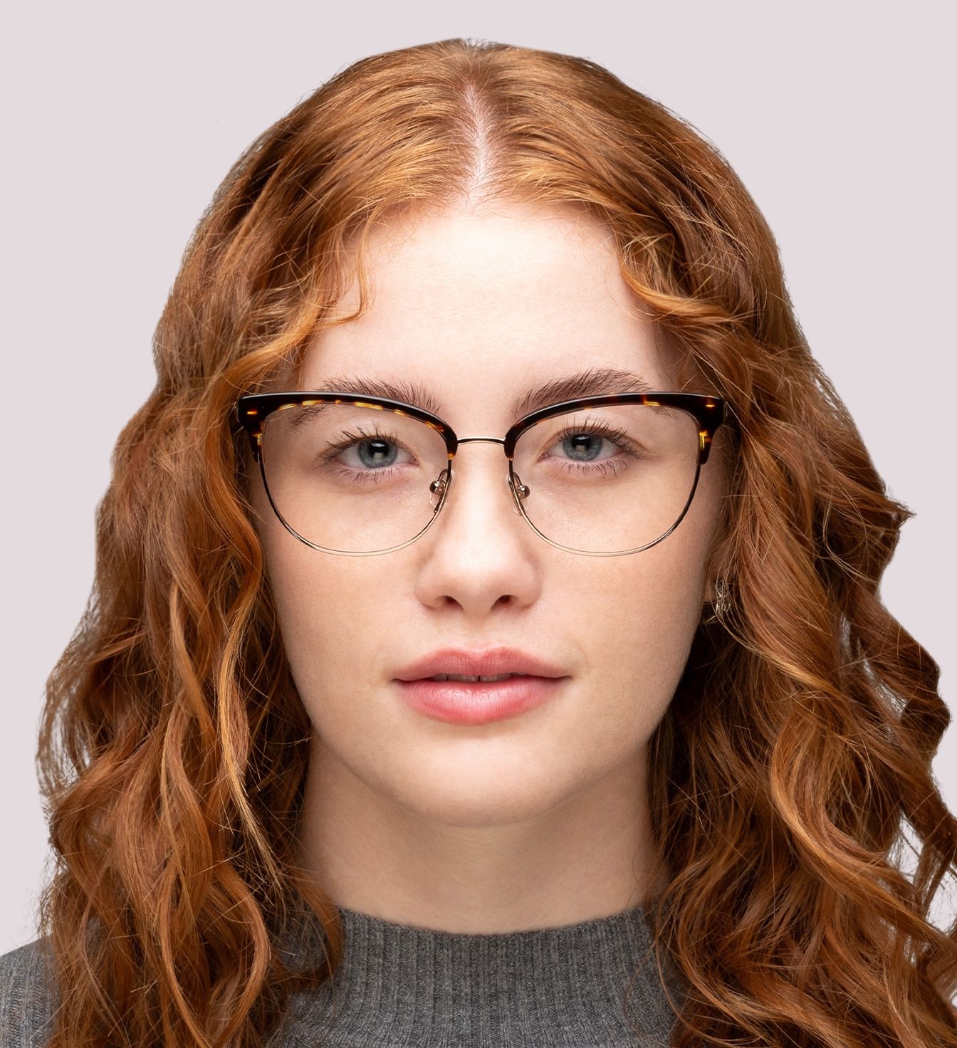A lady with long red wavy hair wearing a tortoise-print oval frame made of acetate with metal rims.