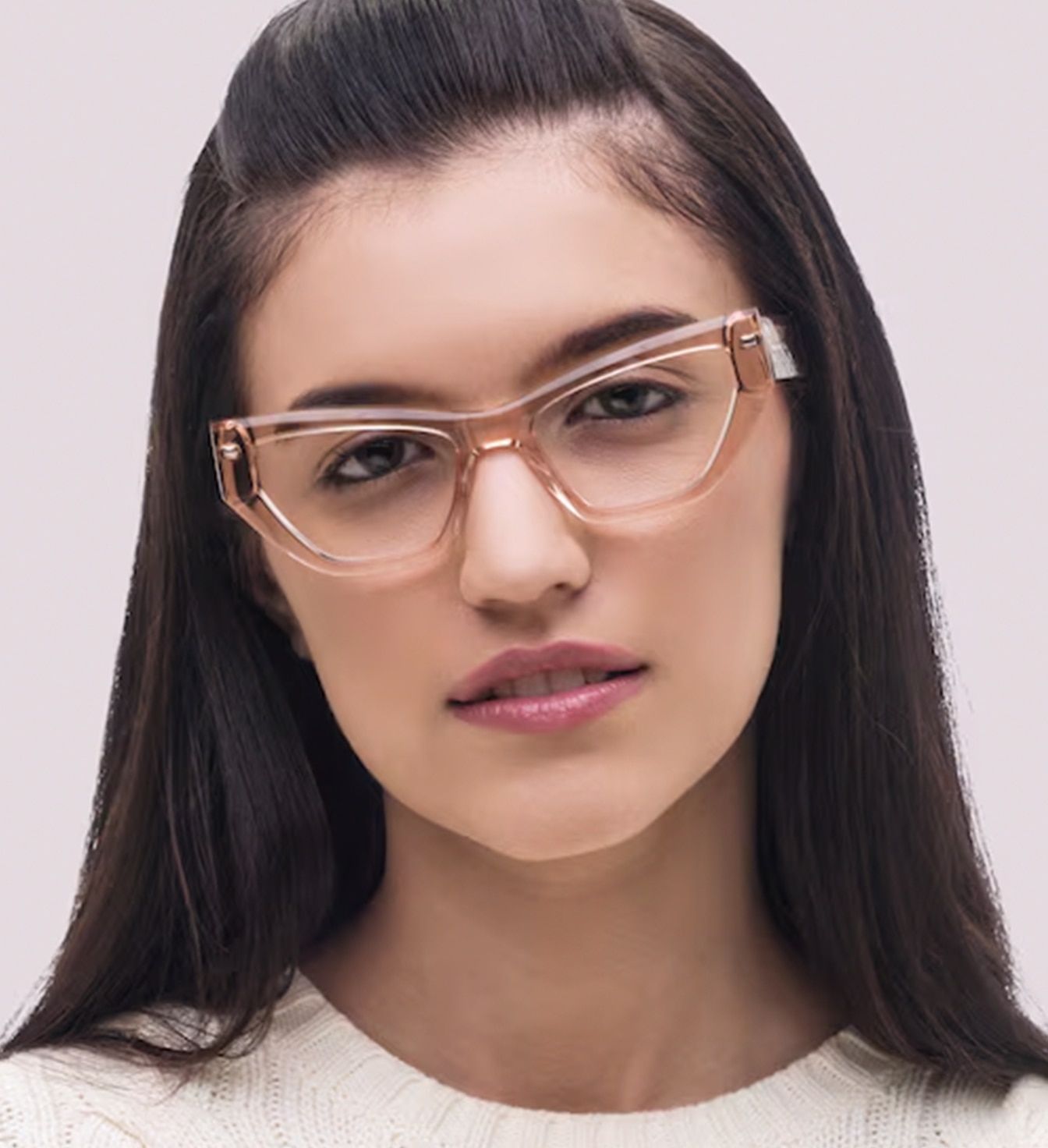 A young lady with long dark hair. Her fridge is clipped back on top of her head. She is smiling slightly, wearing glasses made of transparent peach-coloured acetate.