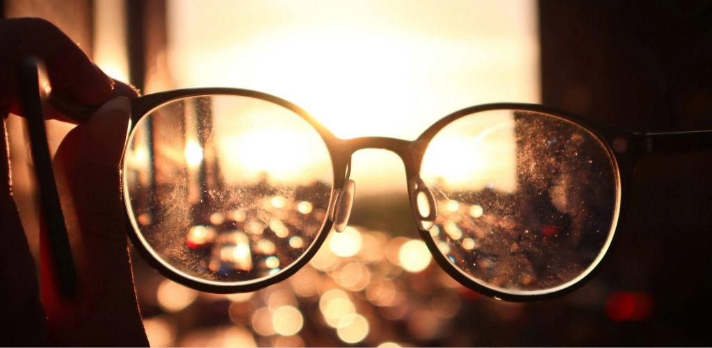 Close-up of dirty, scratched eyeglass lenses with sunlight glare, showing reduced clarity and visibility.