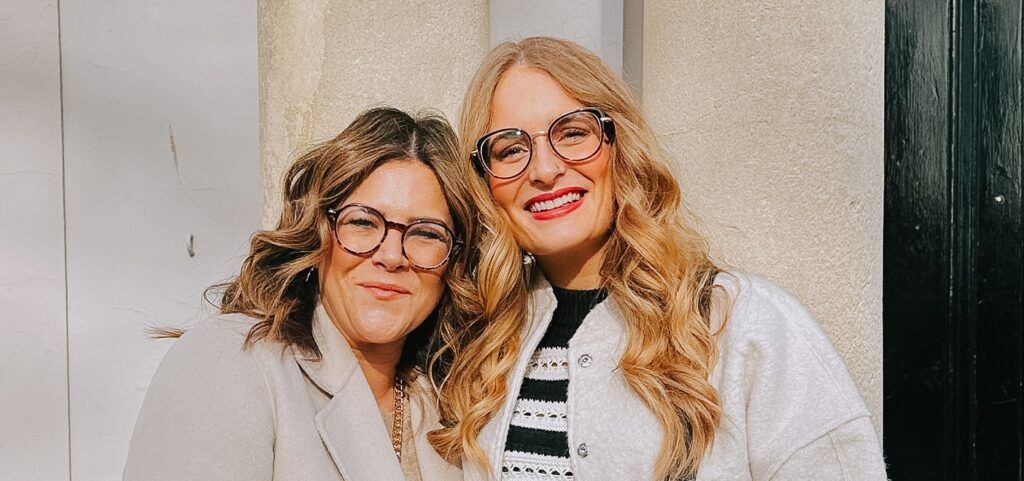 Two female friends shoulder to shoulder smiling for a photo wearing their new frames