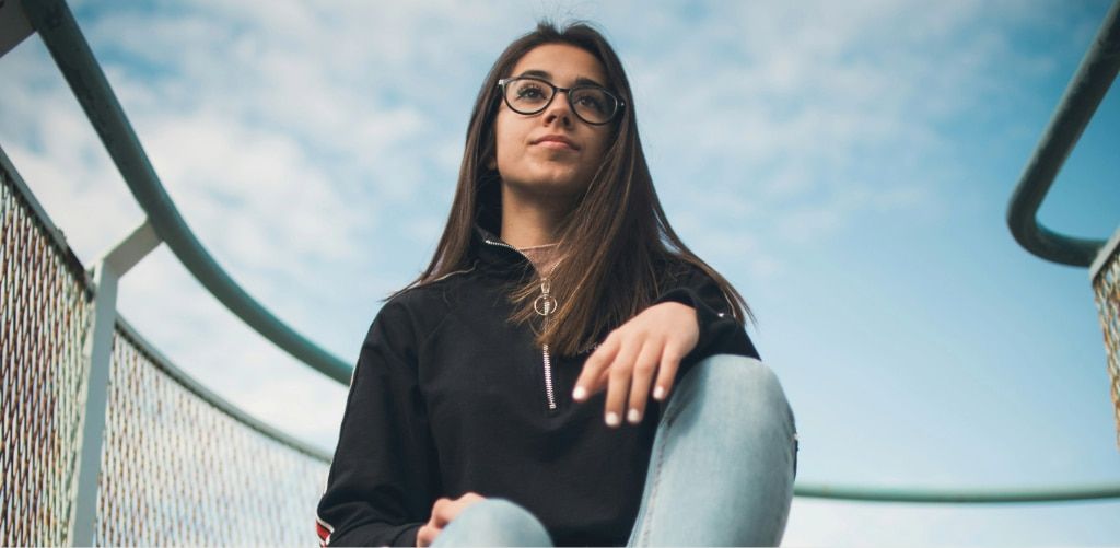 Woman wearing sporty eyeglasses and casual athleisure outfit, sitting outdoors under a bright sky, styled for everyday wear.