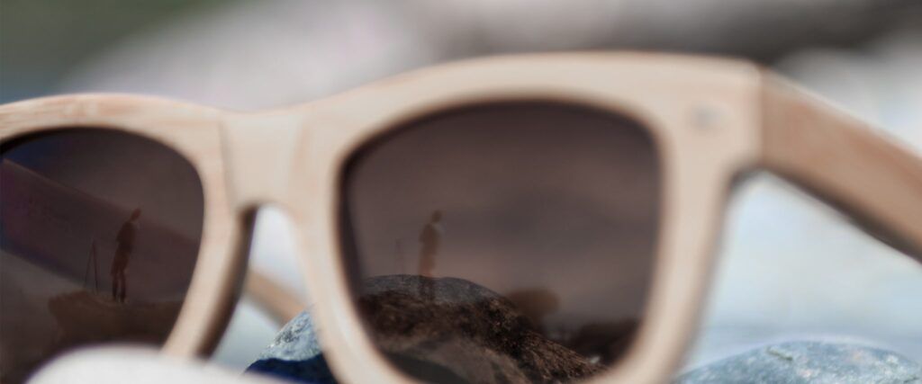 A pair of sunglasses angled to one side with a reflection of a person in the distance.