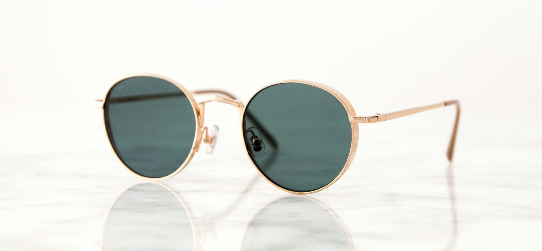 A pair of round, gold-rimmed sunglasses with green lenses lying on a table
