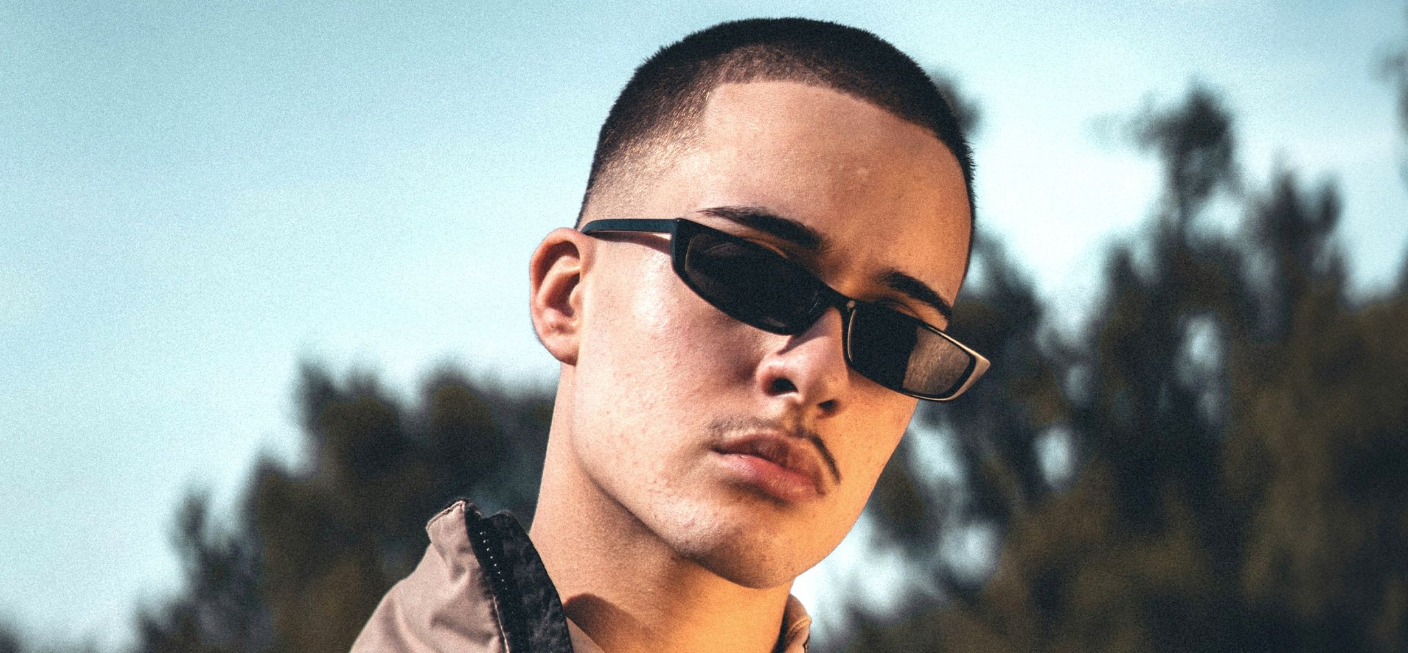 A man with short dark hair and a thin moustache wearing narrow black sunglasses