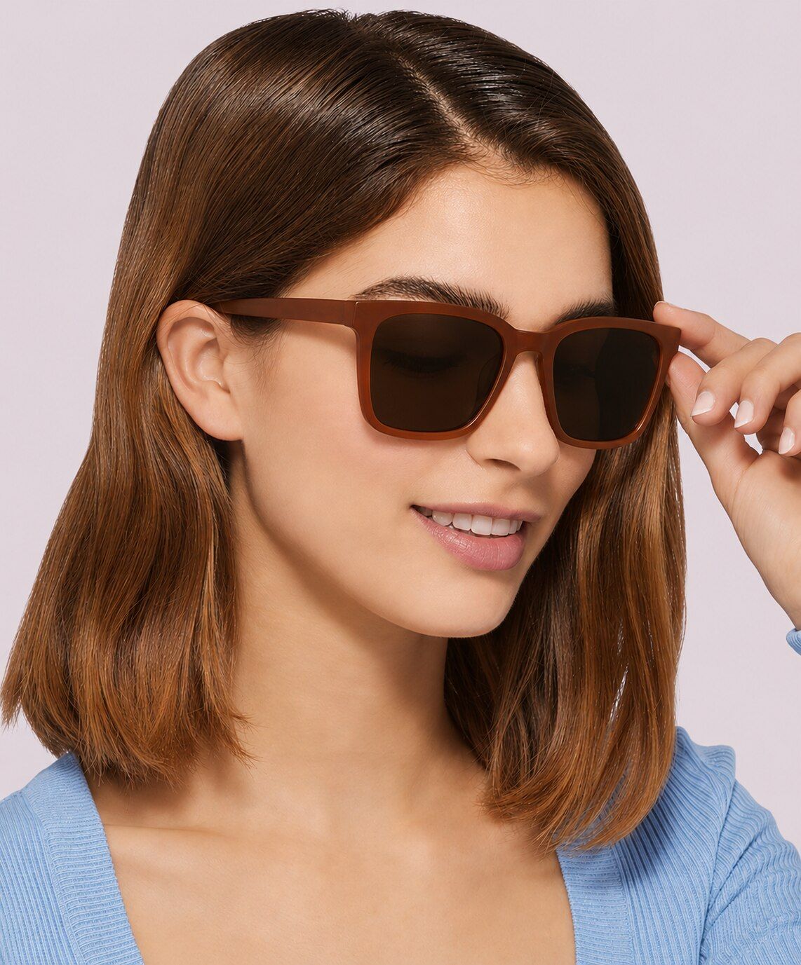 Woman with medium dark-blonde hair wearing a light-blue top and square amber GD Collection Gian prescription sunglasses against a light background.