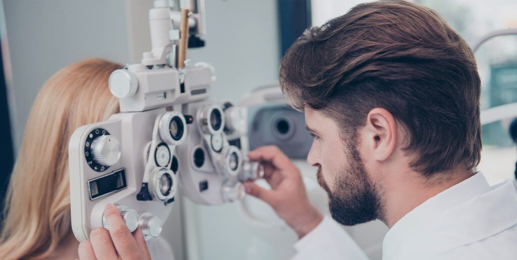 An ophtalmologist adjusts a phoropter while inspecting a woman's eyes