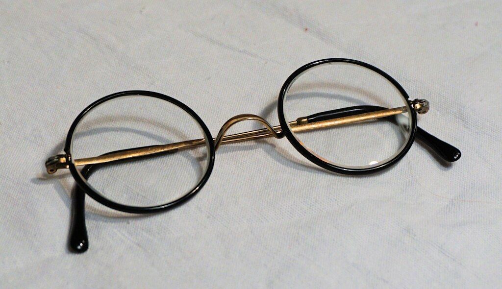A vintage pair of round metal glasses folded on a smooth white piece of linen fabric.